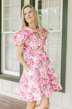 Model wearing a white dress with pink flowers, puff short sleeves and pockets.  