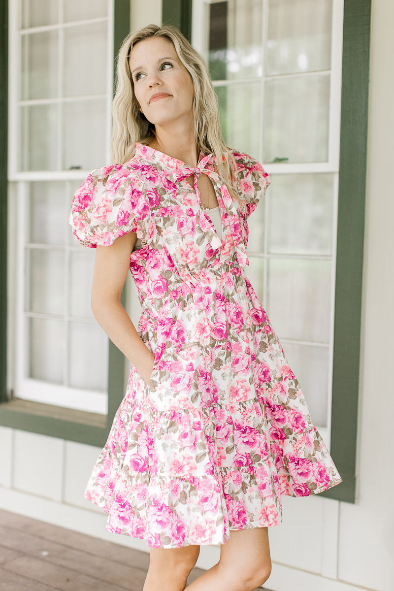 Model wearing a white dress with pink flowers, puff short sleeves and pockets.  