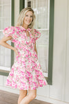 Model wearing a white dress with pink flowers, puff short sleeves and V-neck with a tie.