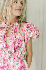 Close up of v-neck with tie and puff short sleeves on a white dress with pink flowers.