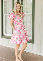 Model wearing sandals with a white dress with pink flowers, bubble short sleeves and pockets.