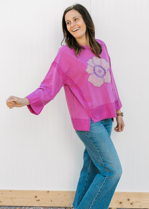 Model wearing a pink top with a stitched rose in the center, 3/4 sleeves and exposed hem. 