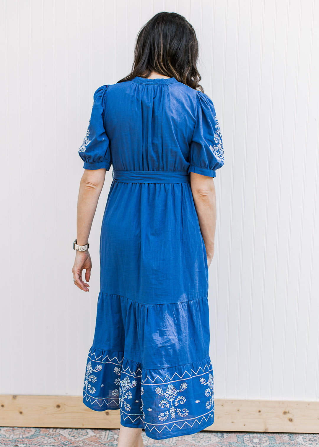 Back view of Model wearing a royal blue midi with cream embroidery, tie at waist and short sleeves.