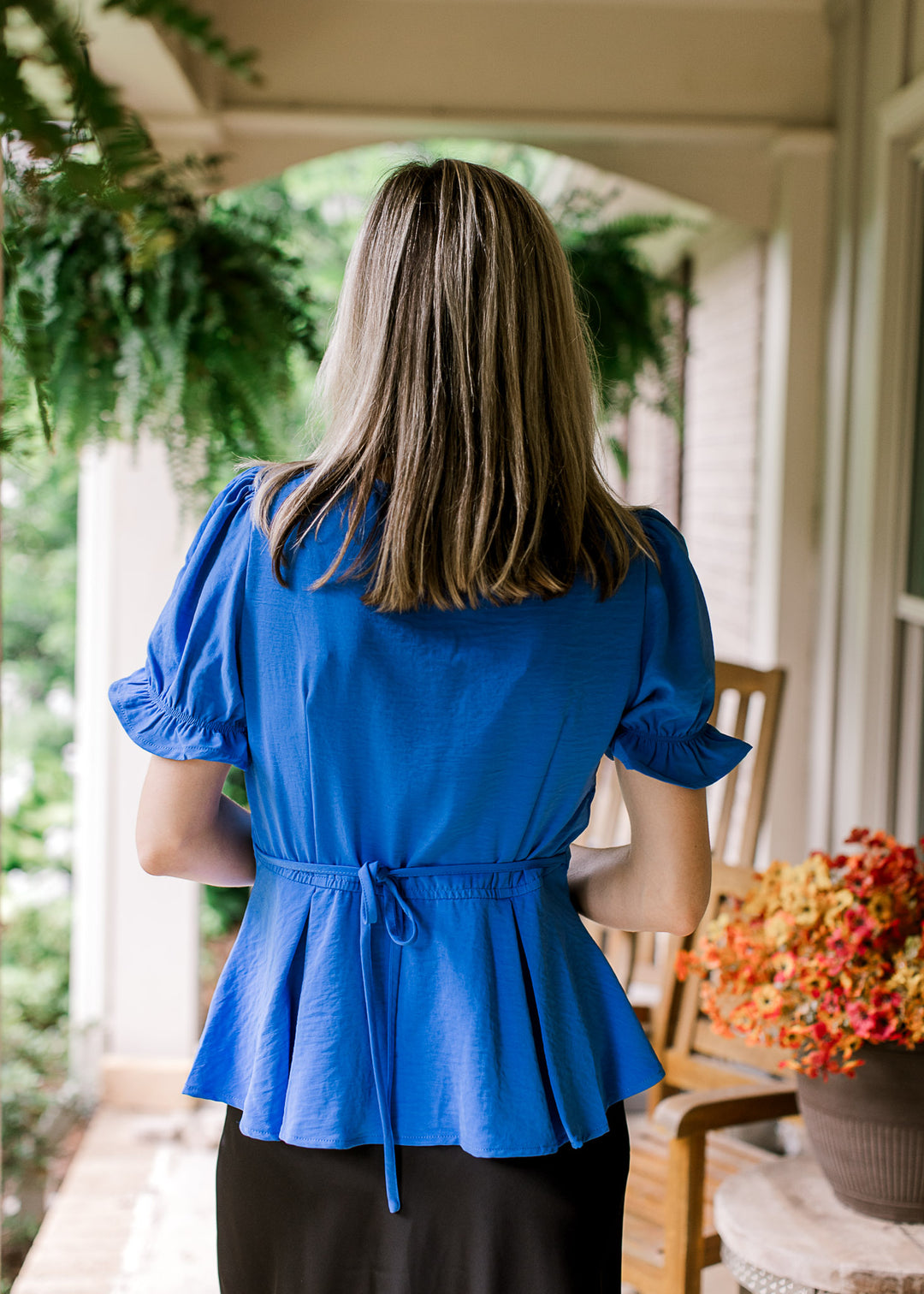 Back view of model wearing a royal blue top with tie back, short sleeves and pleated hem.