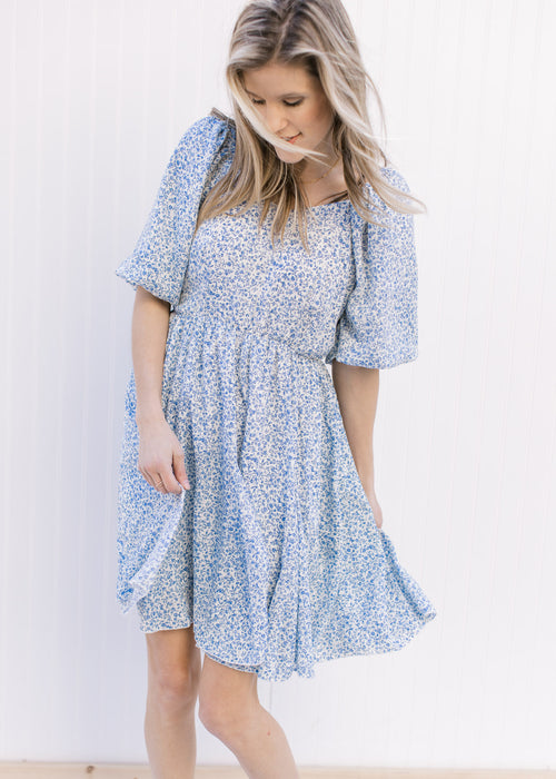 Model wearing a white, above the knee dress with ditsy blue floral design and bubble short sleeves.