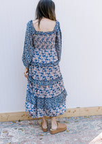 Back view of Model wearing a navy dress with cream flowers, a smocked bodice and square neck.