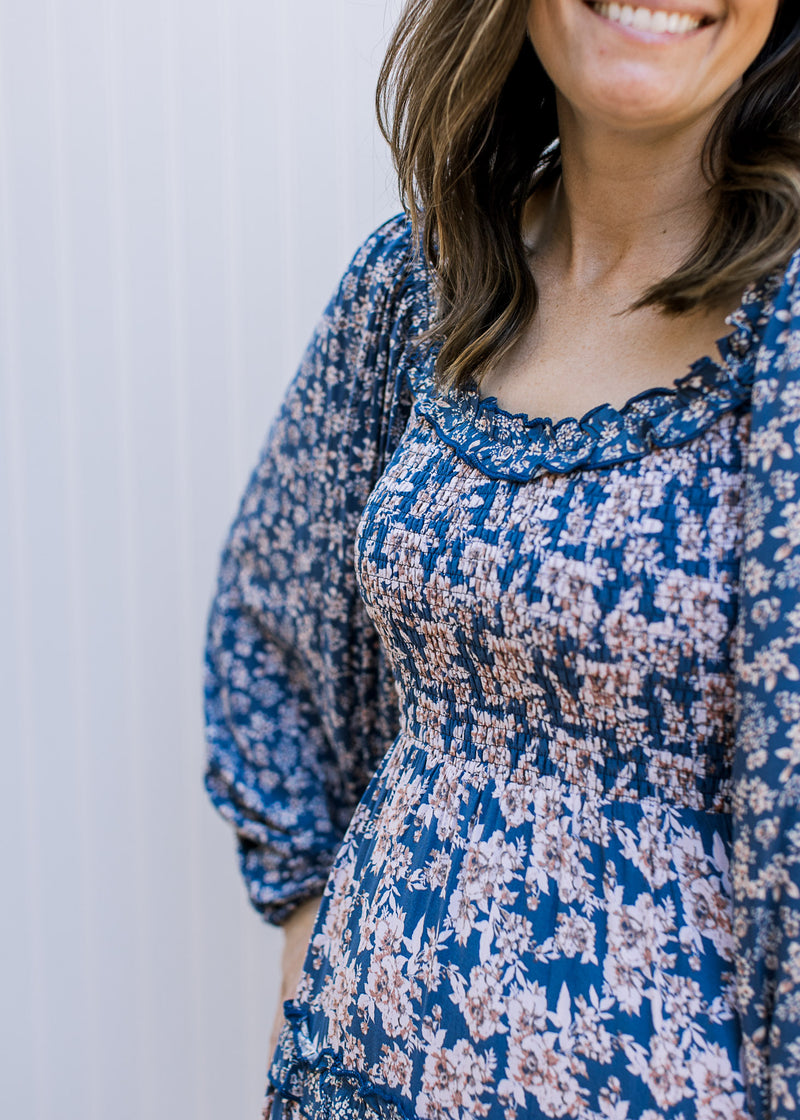 Close up of smocked bodice and ruffle detail around the neck of a navy maxi with cream flowers.