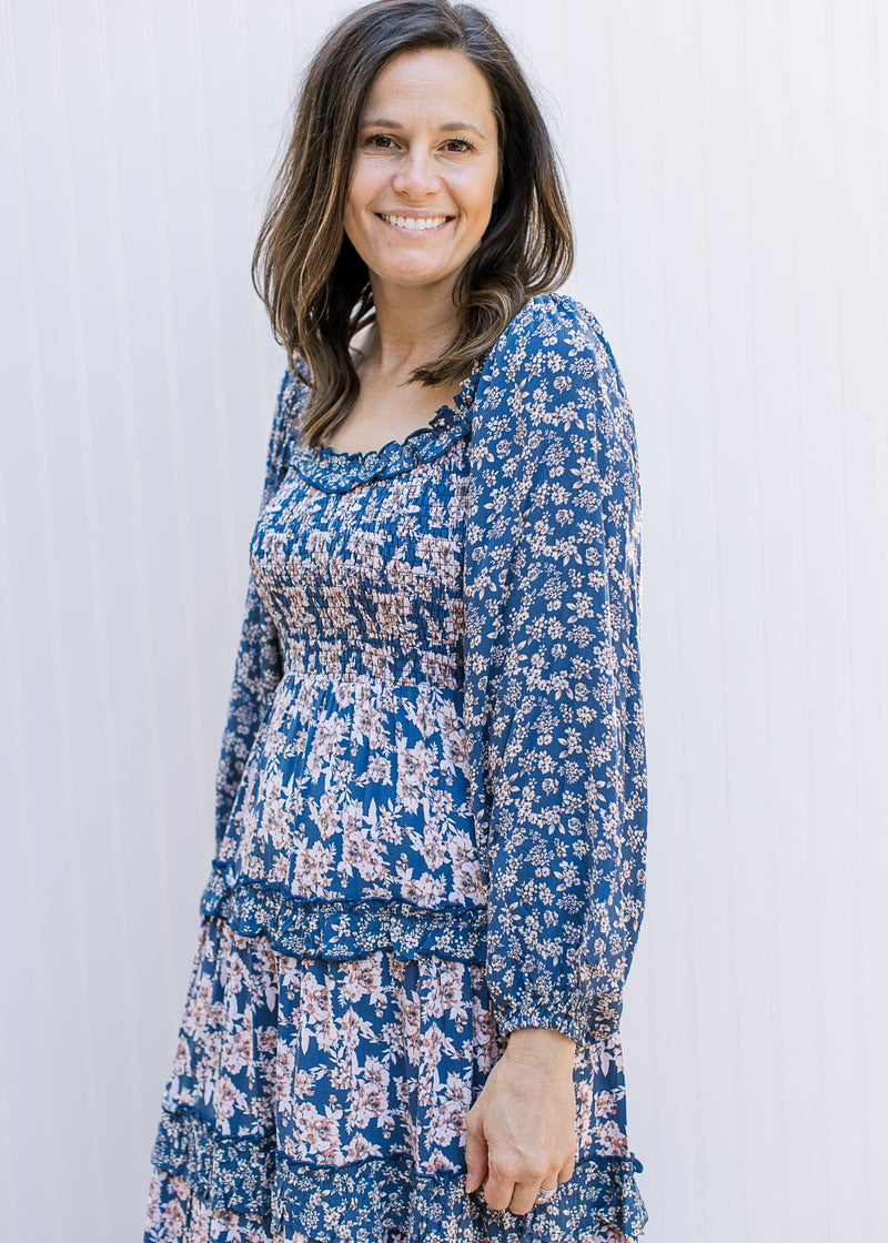 Model wearing a navy dress with cream flowers, a smocked bodice and tiered skirt.