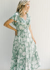 Model wearing a sage v-neck maxi dress with a cream floral design and a ruffle cap sleeve. 