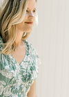 Close up view of v-neck on a model wearing a sage dress with a cream floral design. 