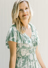 Close up view of a model wearing a sage dress with a cream pattern, ruffle sleeve and elastic waist