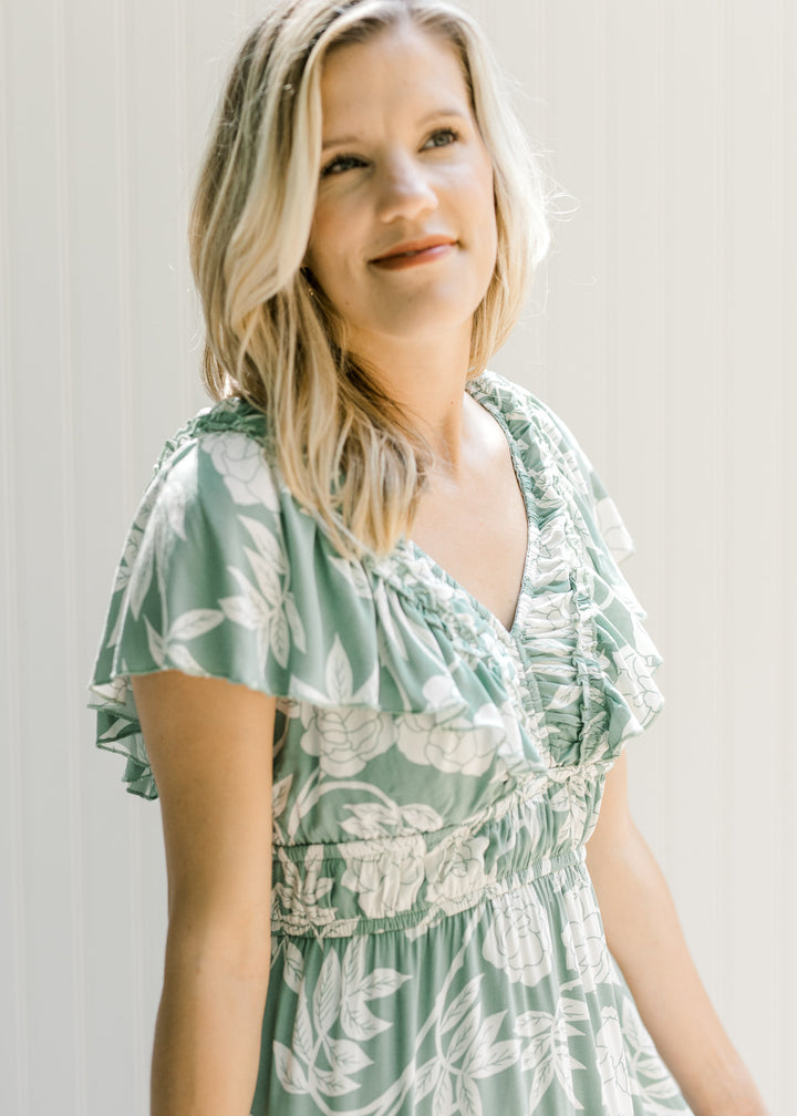 Close up view of a model wearing a sage dress with a cream pattern, ruffle sleeve and elastic waist