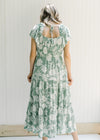 Back view of Model wearing a sage v-neck maxi dress with a cream floral design and a ruffle sleeve. 