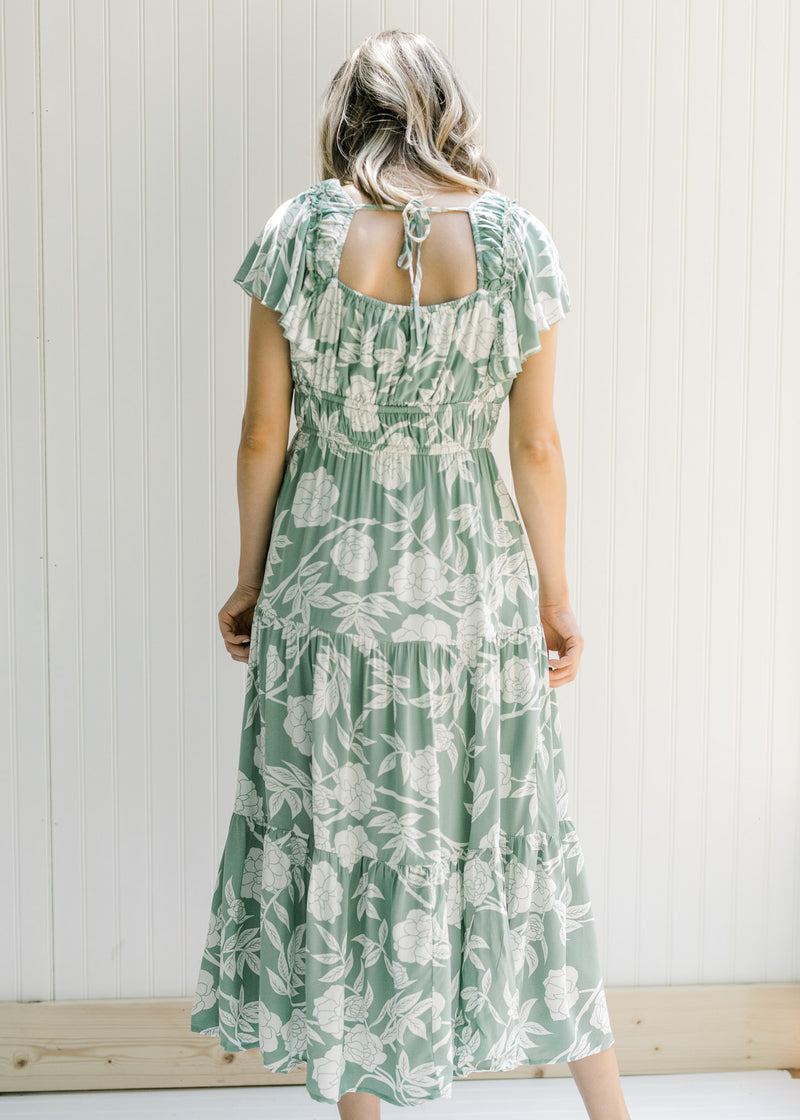 Back view of Model wearing a sage v-neck maxi dress with a cream floral design and a ruffle sleeve. 