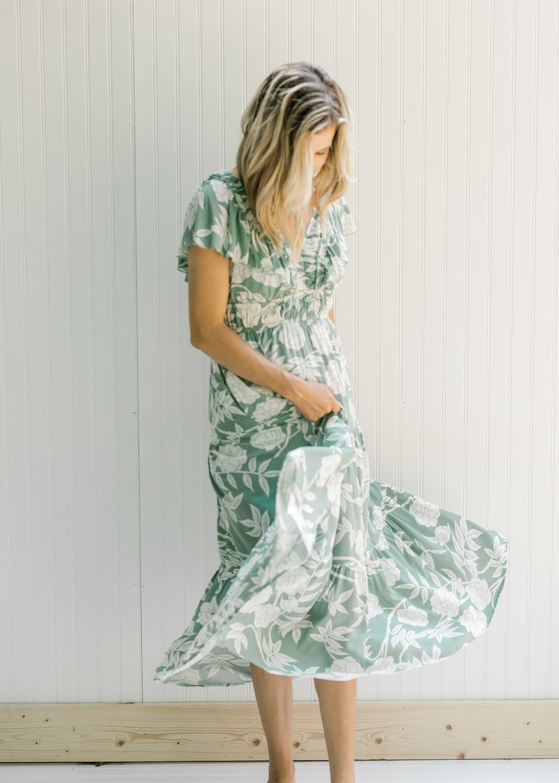 Model twisting in a sage v-neck maxi dress with a cream floral design and a ruffle cap sleeve. 
