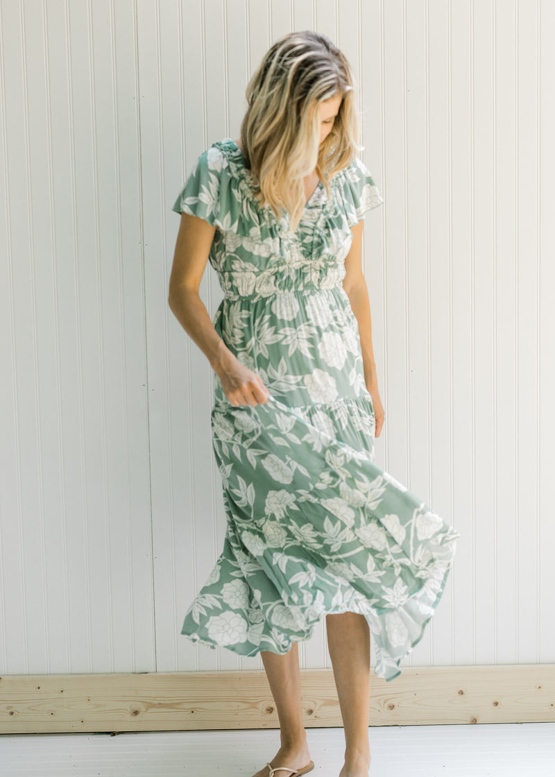 Model twisting in a sage v-neck maxi dress with a cream floral design and a elastic waistband.