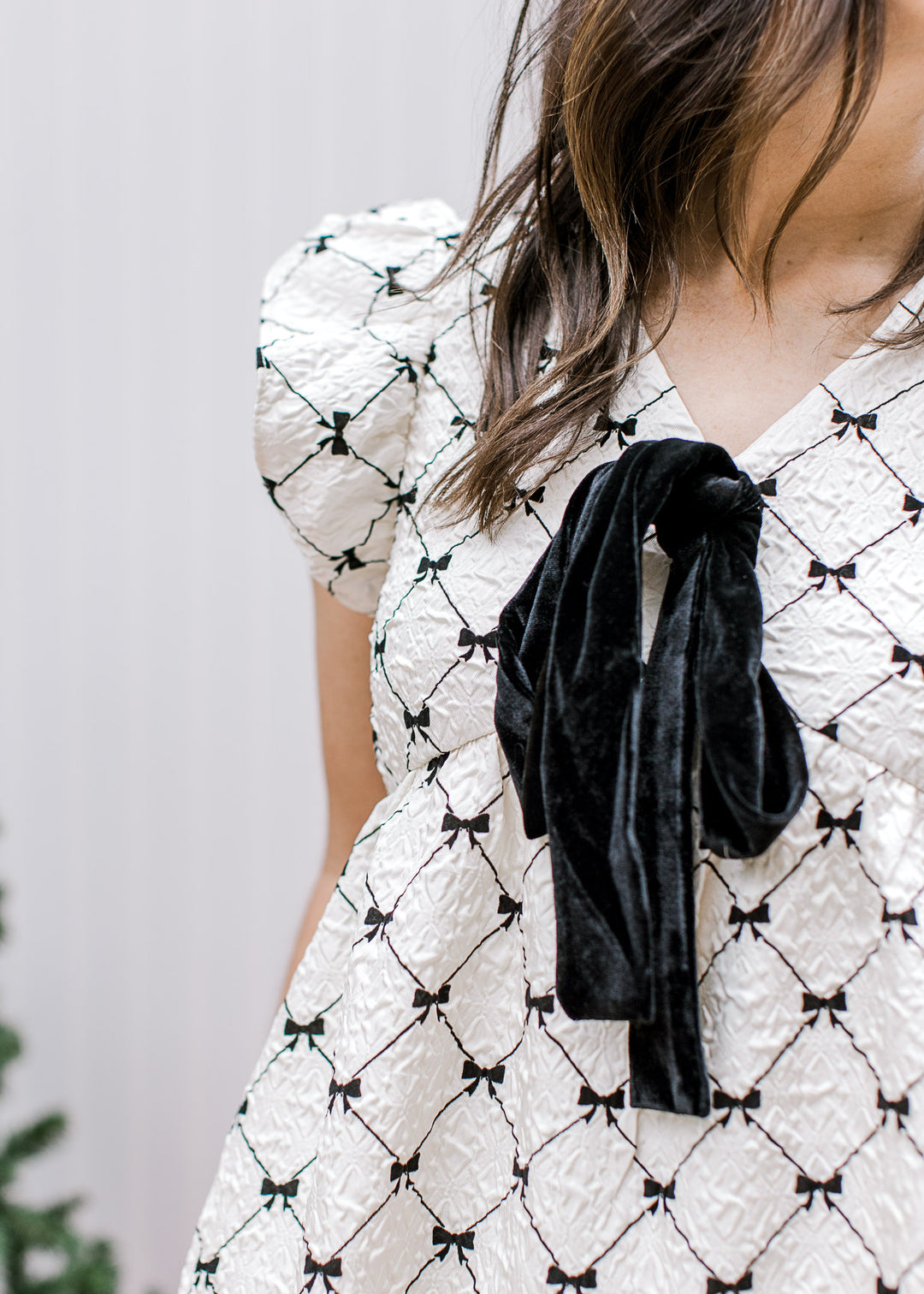Close up of black tie at v-neck on a cream dress with black diamonds, pockets and flutter sleeves. 