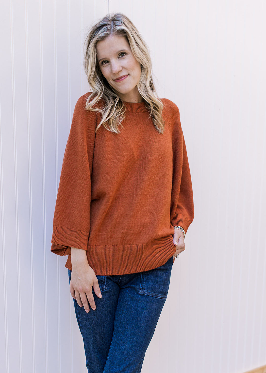 Model wearing a rust sweater with 3/4 sleeves, round neck and ribbed neck, hem and cuff. 