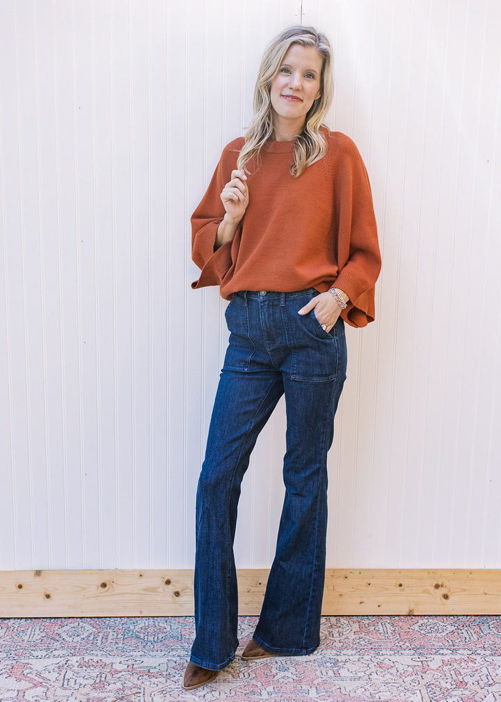 Model wearing jeans, boots and a rust sweater with 3/4 sleeves, round neck and ribbed detailing.