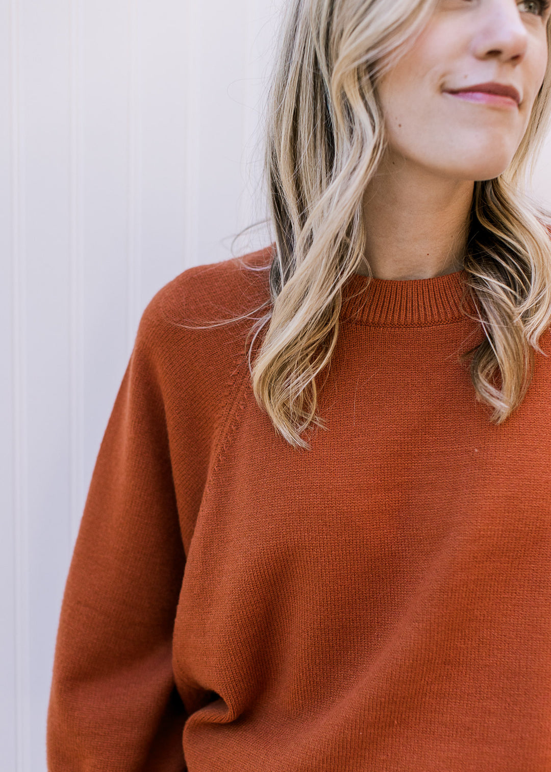 Close up of round ribbed neckline on a rust sweater with 3/4 sleeves and an oversized fit. 