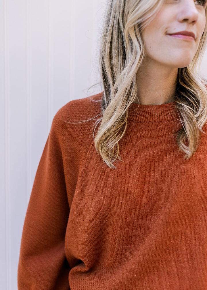 Close up of round ribbed neckline on a rust sweater with 3/4 sleeves and an oversized fit. 