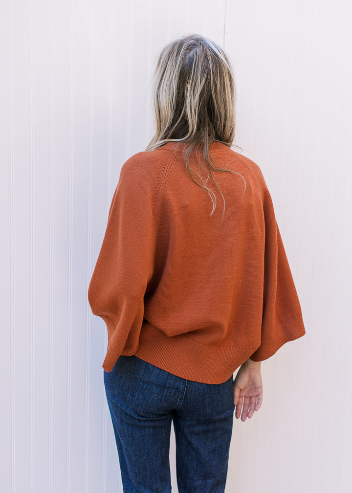 Back view of Model wearing a rust sweater with 3/4 sleeves, round neck and ribbed detail. 