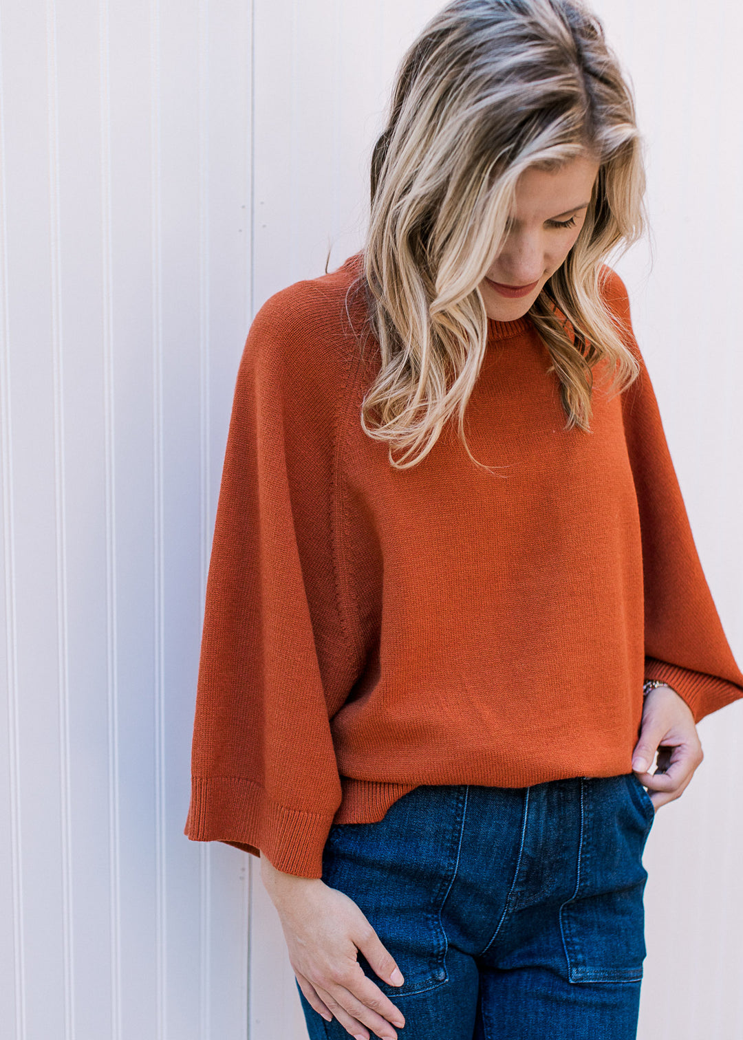 Model wearing a cozy rust sweater with 3/4 sleeves, round neck and ribbed neck, hem and cuff. 