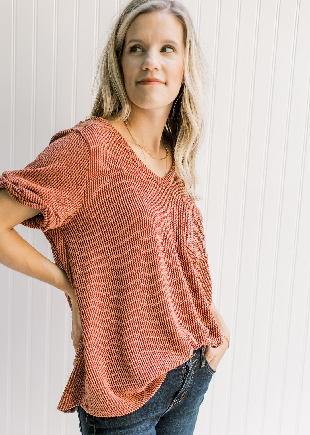 Model wearing a rust v-neck top with a corded material, patch pocket and cuffed short sleeves. 