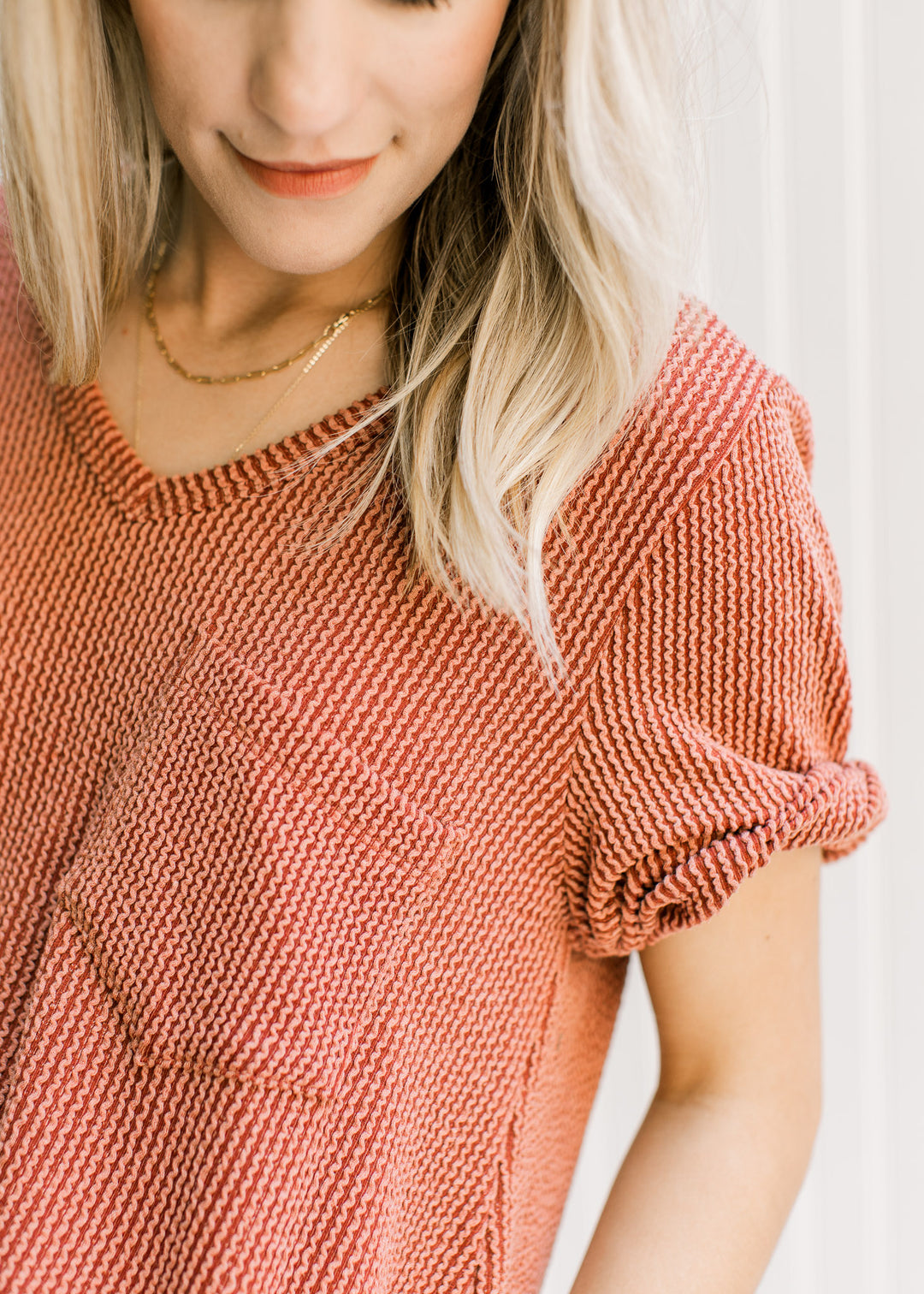 Close up of patch pocket and cuffed short sleeves on a v-neck rust colored tee. 