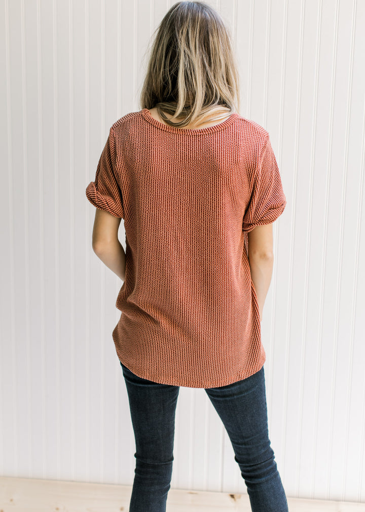 Back view of rust v-neck top with a corded material, patch pocket and cuffed sleeves. 
