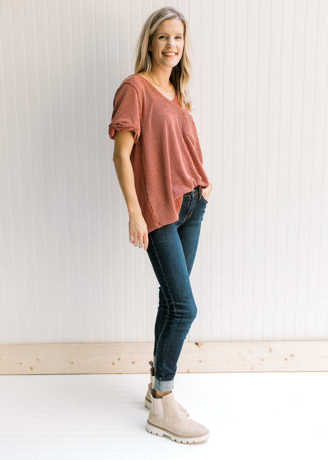Model wearing jeans, booties and a rust v-neck top with a corded material and cuffed short sleeves.