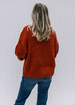 Back view of a model wearing a rust cardigan with white and yellow embroidered daisies on the front.