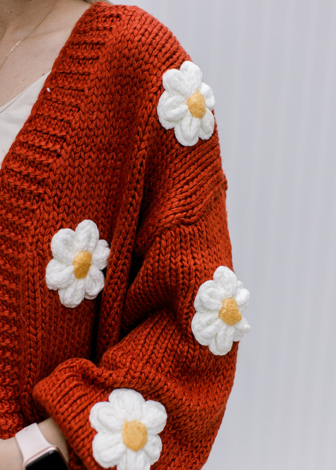 Close up of white and yellow embroidered daisies and ribbed detail on a rust cardigan. 
