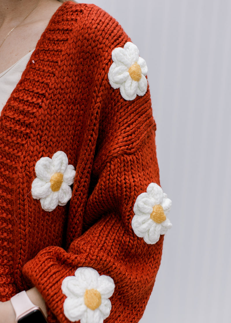 Close up of white and yellow embroidered daisies and ribbed detail on a rust cardigan. 