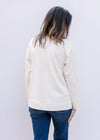 Back view of Model wearing a cream top with rust flowers on front, long sleeves and a round neck. 