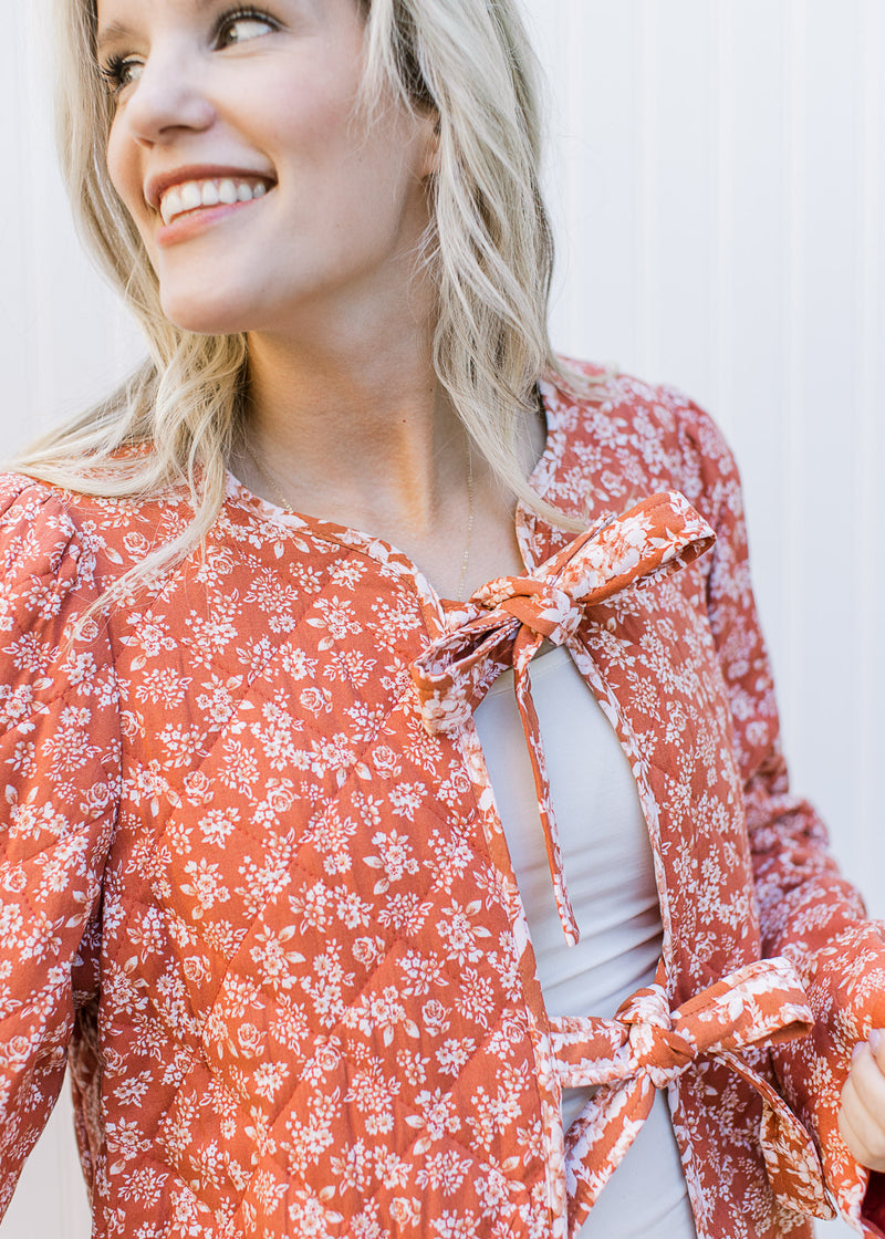 Close up of two tie closure on a rust colored jacket with cream flowers and long sleeves. 