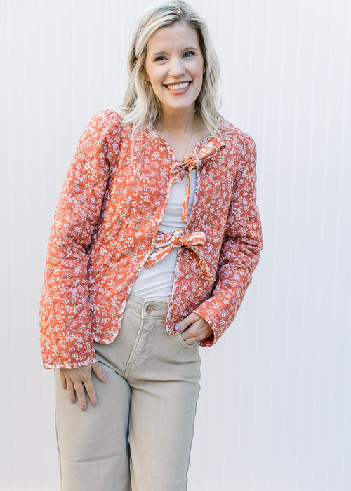 Model wearing a rust jacket with cream flowers, quilted material and two tie closure. 