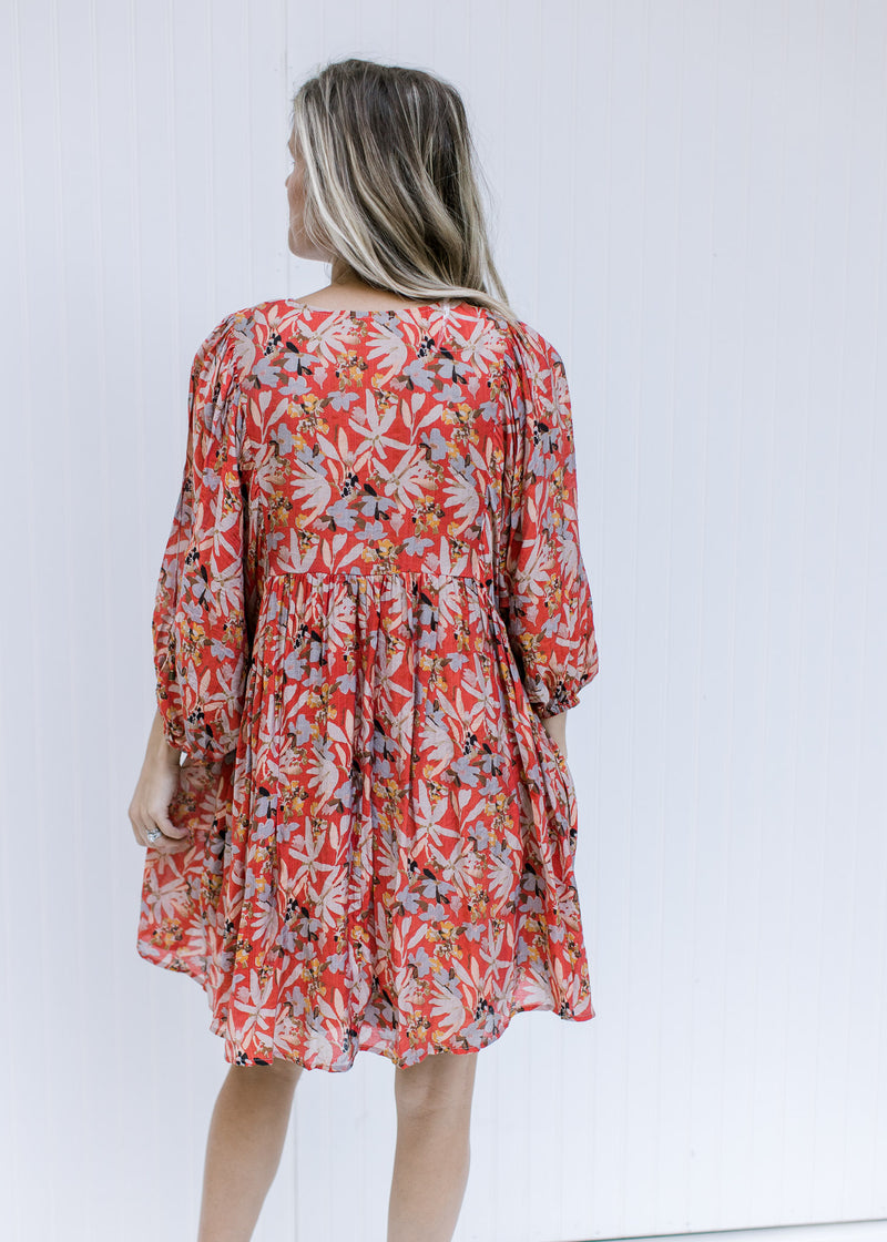 Back view of Model wearing a rust above the knee dress with 3/4 sleeves and a v-neck with a tie. 