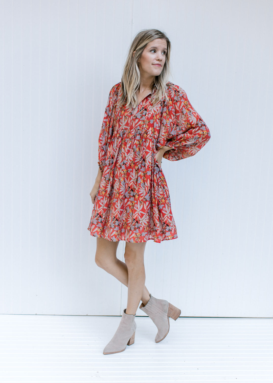 Model wearing booties with a rust above the knee dress with 3/4 sleeves and a v-neck with a tie. 