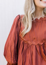 Close up of ric-rac detail and pleated shoulder on a rust colored top with 3/4 sleeve. 