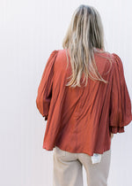 Back view of Model wearing a rust top with ric-rac detail, round neck and poet 3/4 sleeve. 