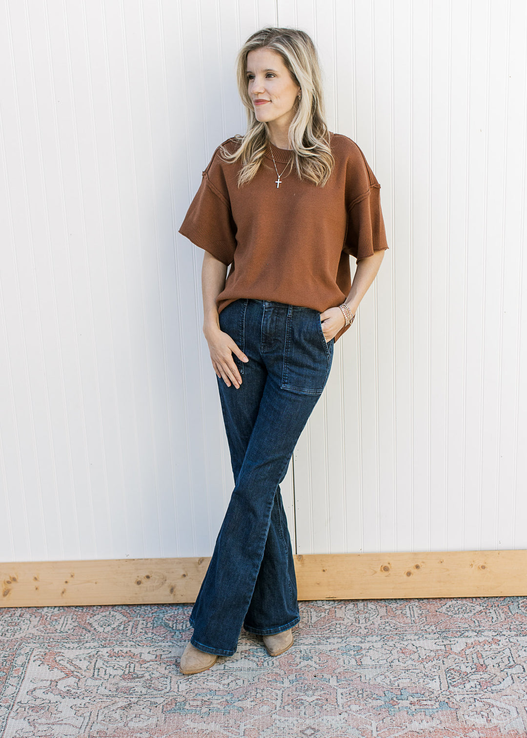 Model wearing jeans, boots and a rust top with exposed hem, round neck and rolled hem.