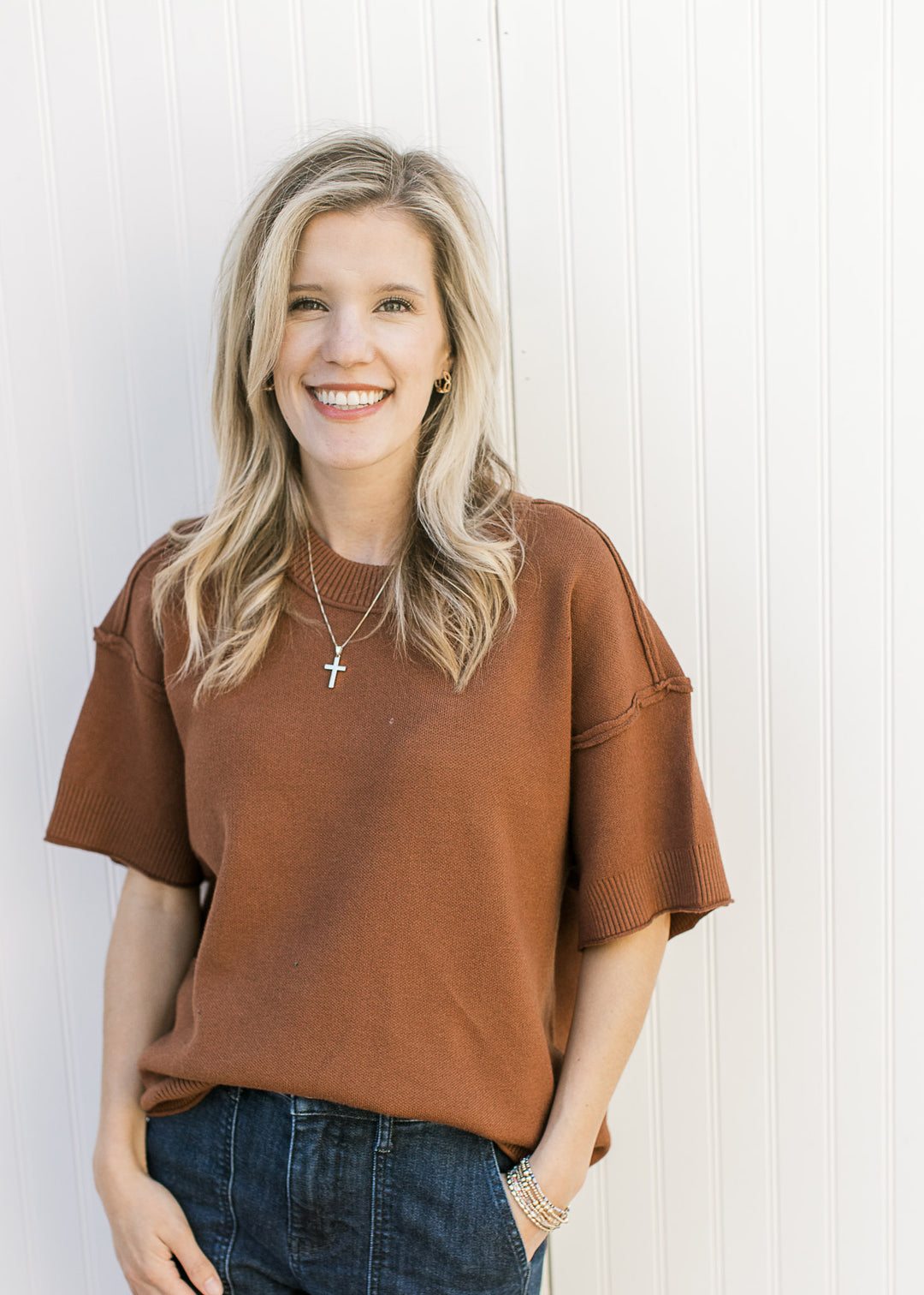 Model wearing a rust top with exposed hem, round neck, rolled hem and ribbed detail. 