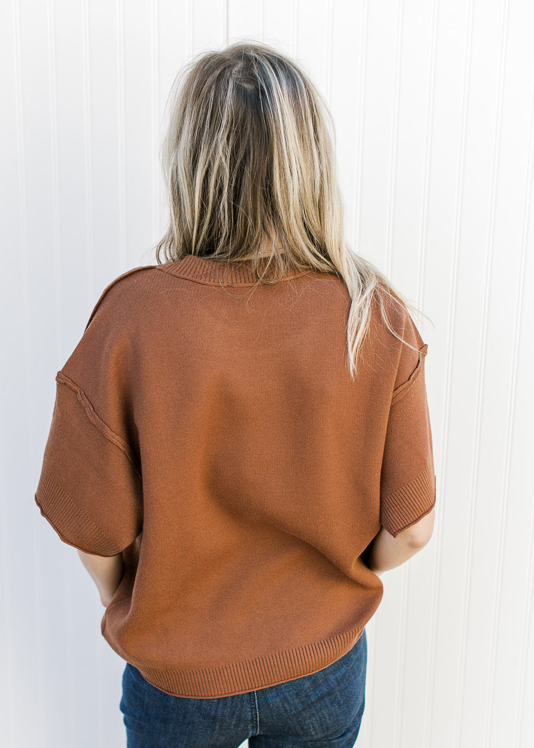 Back view of Model wearing a rust top with exposed hem, round neck, rolled hem and ribbed detail. 