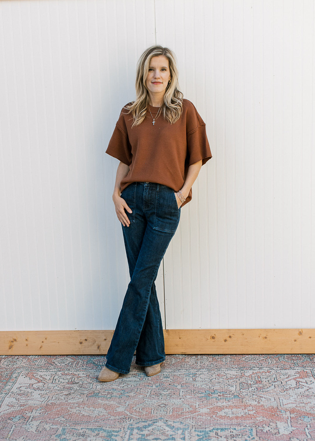 Model wearing jeans and a rust top with exposed hem, round neck, rolled hem and ribbed detail. 