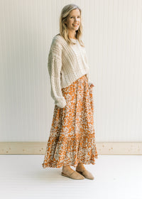 Model wearing a cream top and a rust colored maxi with a cream leaf pattern and an elastic waist.