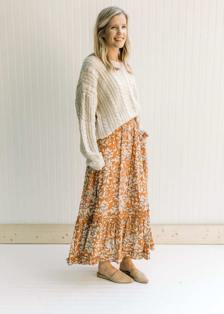 Model wearing a cream top and a rust colored maxi with a cream leaf pattern and an elastic waist.