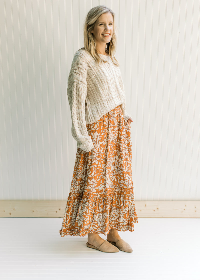 Model wearing a cream top and a rust colored maxi with a cream leaf pattern and an elastic waist.