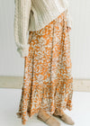 Model wearing a rust colored maxi skirt with a cream leaf pattern, elastic waist and pockets. 