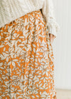 Close up of rust colored midi skirt with a cream leaf pattern, elastic waistband, pockets and rayon.